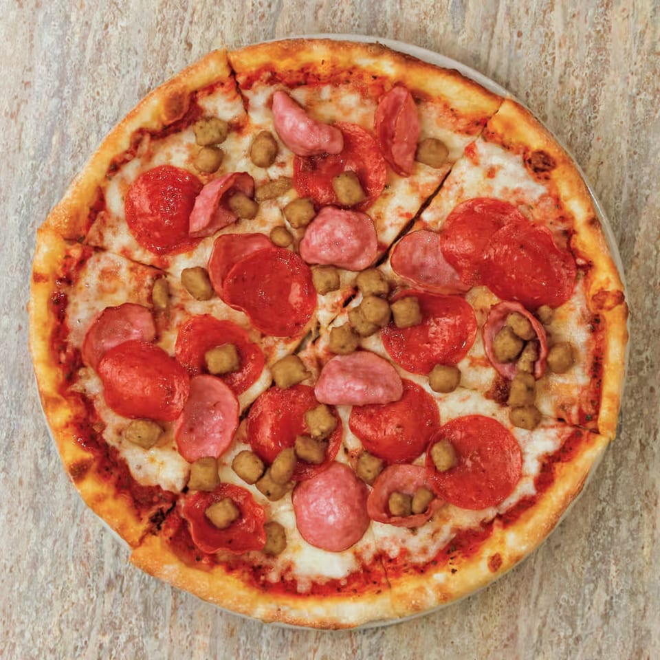 Pastafina's pepperoni, sausage, and ham pizza, sliced and ready to eat.