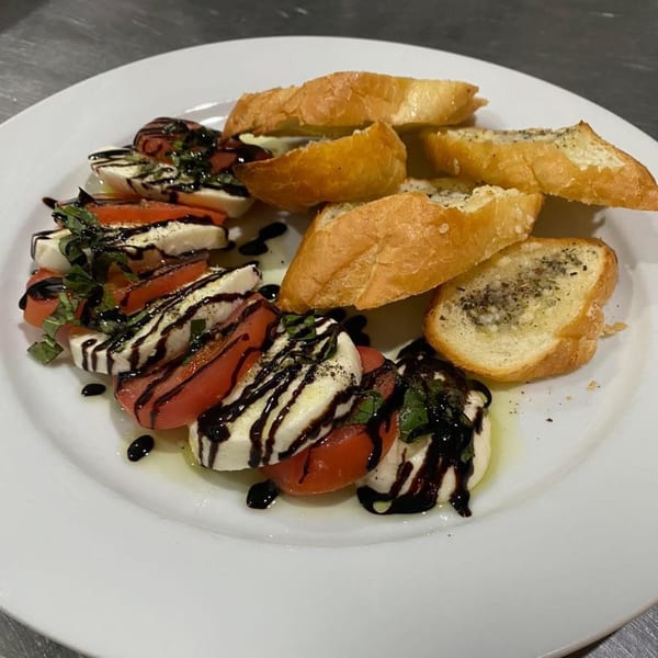 Caprese salad with sliced tomatoes, mozzarella, basil, balsamic glaze, and garlic bread on a white plate.