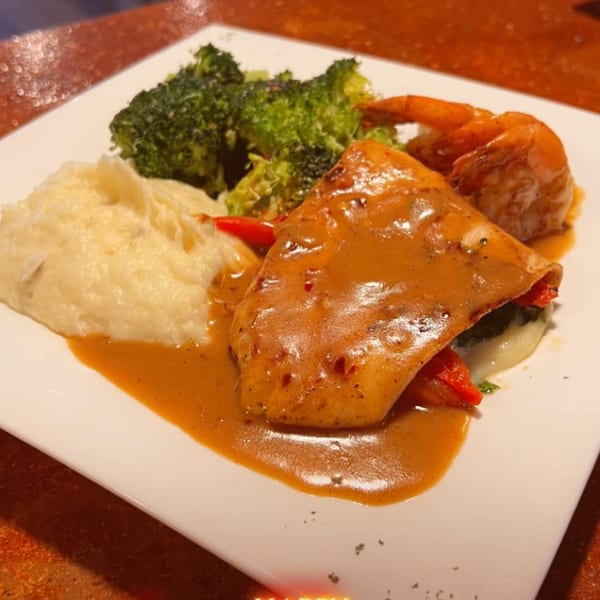 Pastafina's chicken dish with creamy sauce, mashed potatoes, broccoli, and shrimp on a white plate.