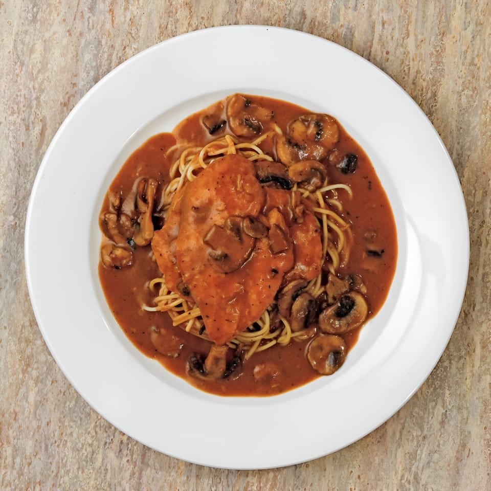 Pastafina's chicken marsala with mushrooms and spaghetti in a rich brown sauce on a white plate.